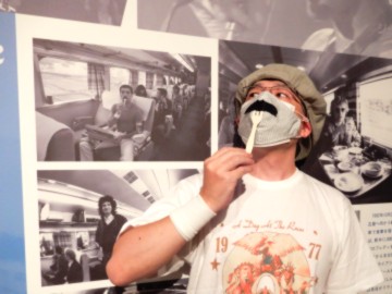 新幹線で駅弁を食べるフレディの写真の前で、新幹線で駅弁を食べるフレディの仮装をする人間